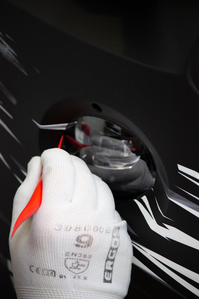 White-gloved hands carefully apply a red racing decal on a black car surface.